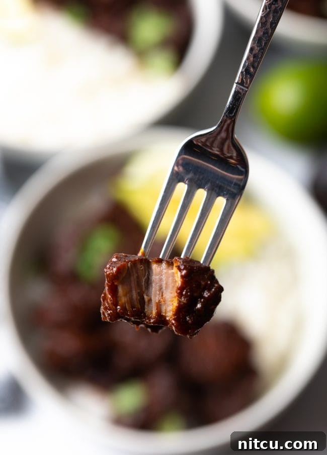 The Ultimate Carne Adovada Recipe 4 fork holding piece of red chile simmered pork with bite