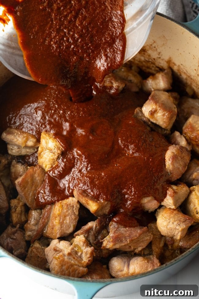 The Ultimate Carne Adovada Recipe 9 adding the smoky sauce to the chunks of seared pork in the pot