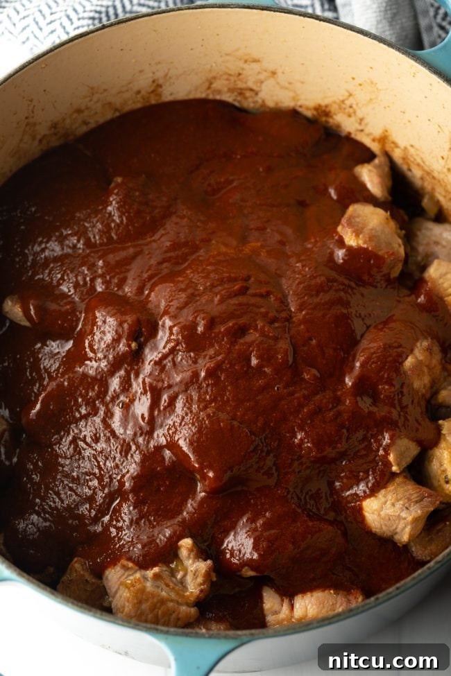 The Ultimate Carne Adovada Recipe 10 seared pork covered in red chile sauce in a pot