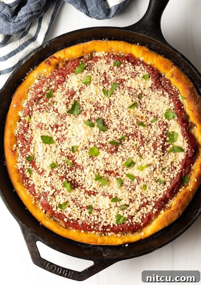 Iron-Clad Deep Dish Delight 11 A beautiful top view of a baked Chicago-style pizza, freshly garnished with grated Parmesan cheese and vibrant green parsley, ready to be served.