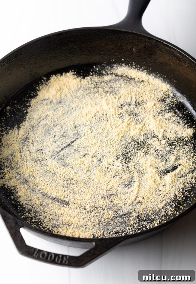 Iron-Clad Deep Dish Delight 4 A cast iron skillet generously dusted with golden cornmeal, prepared and ready to receive the pizza dough for a homemade deep dish pizza.