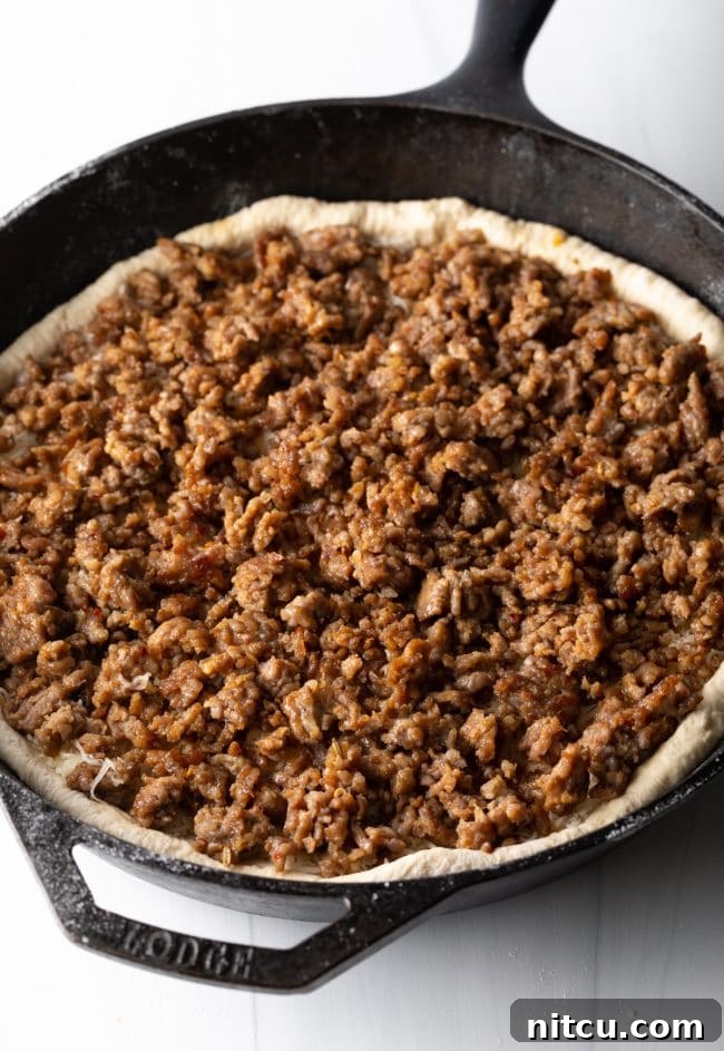 Iron-Clad Deep Dish Delight 6 Perfectly browned Italian sausage crumbles layered over the melted cheese and pizza dough, creating a hearty filling for the deep dish pizza.