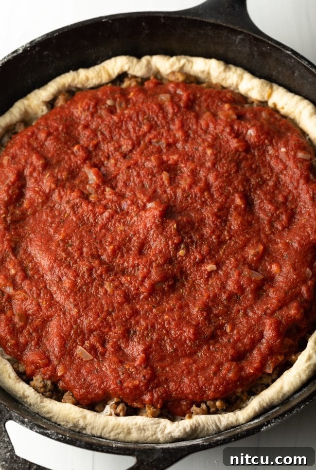 Iron-Clad Deep Dish Delight 7 Thick, chunky tomato sauce spread generously over the browned sausage and cheese layers, completing the traditional Chicago deep dish pizza assembly.