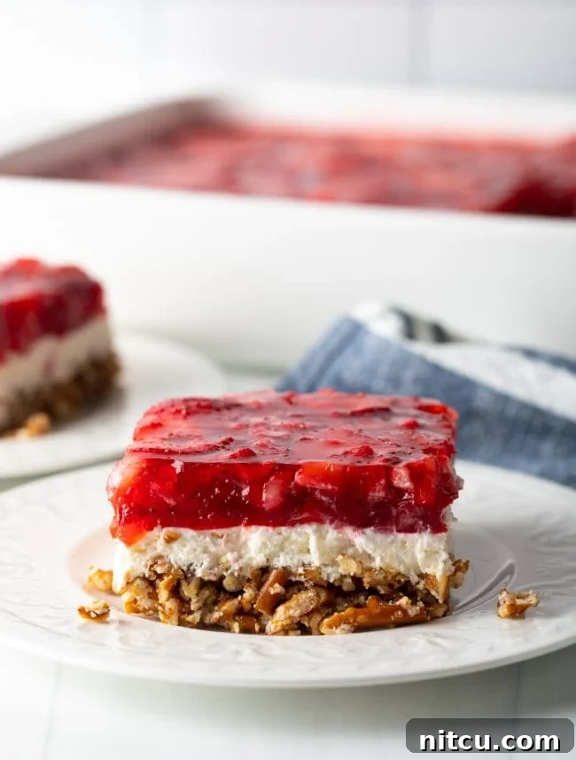 Sweet Strawberry Pretzel Delight 2 Close-up slice of layered strawberry pretzel salad on a white plate, showcasing the distinct pretzel, cream cheese, and jello layers.