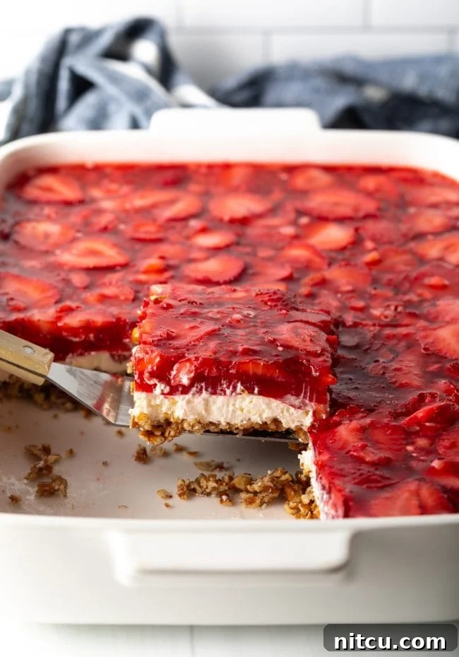 Sweet Strawberry Pretzel Delight 13 A spatula lifting a perfect piece of strawberry pretzel salad dessert from the baking pan, showing the distinct layers.
