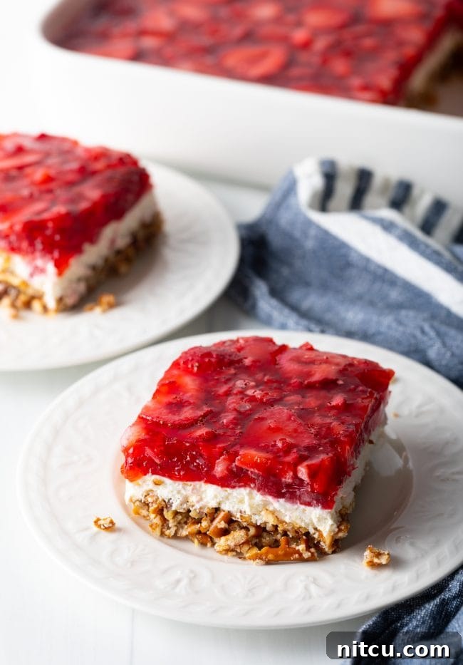 Sweet Strawberry Pretzel Delight 15 Side view of a perfectly square piece of strawberry pretzel salad recipe on a white plate, showing all three layers.