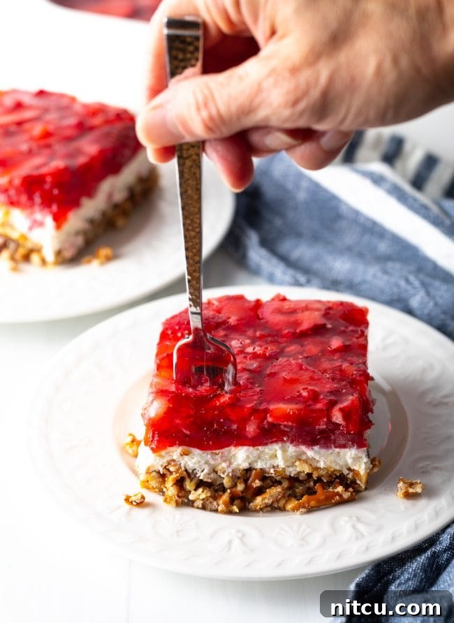 Sweet Strawberry Pretzel Delight 16 A hand with a fork taking a bite of the layered strawberry jello, cream cheese, and pretzel pecan crust dessert.