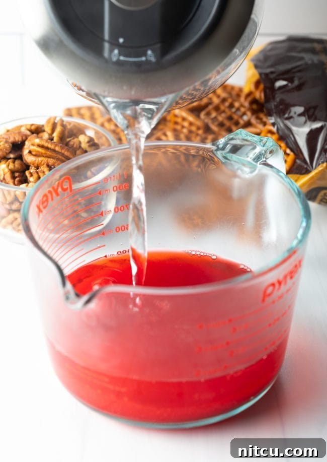 Sweet Strawberry Pretzel Delight 5 A hand pouring hot water into a bowl containing strawberry gelatin mix.