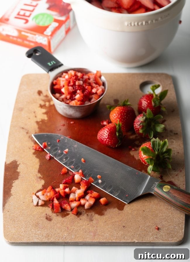 Sweet Strawberry Pretzel Delight 9 A cutting board with a large knife and both whole and diced strawberries, prepared for the dessert.
