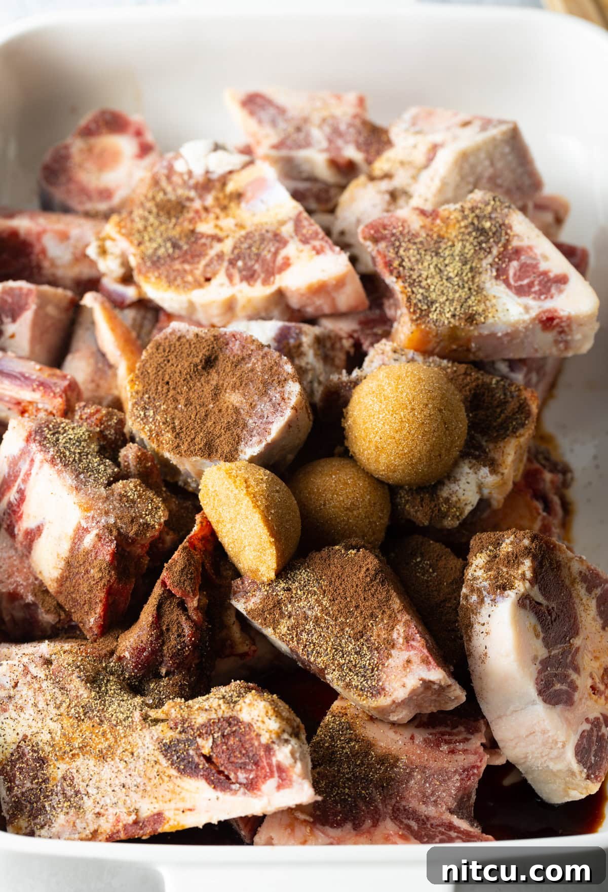 Raw pieces of oxtail in a large cooking pot, seasoned generously with spices and brown sugar, ready for browning.