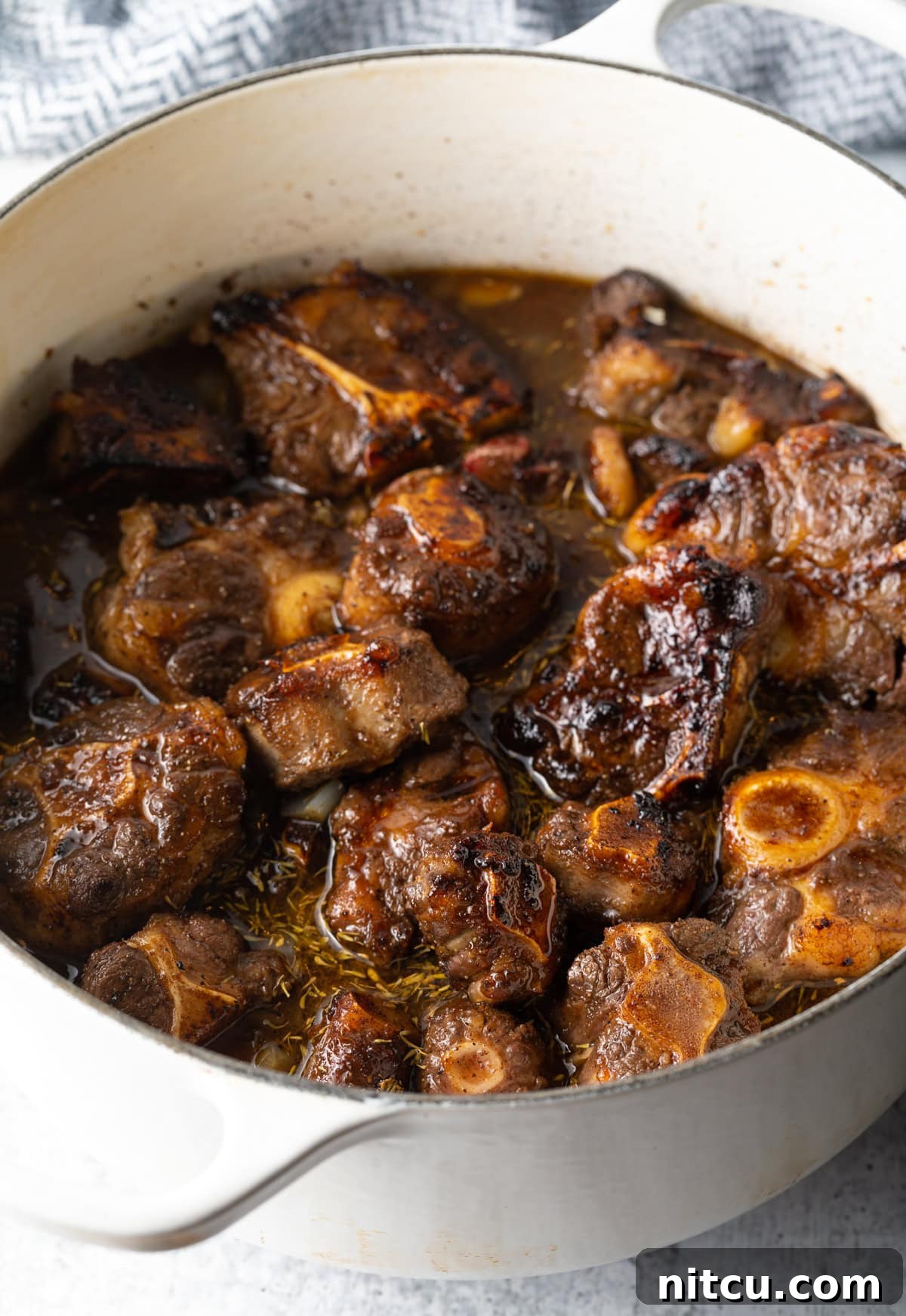 Close-up of oxtail stew simmering in a pot on the stovetop, showcasing the rich gravy and tender meat.