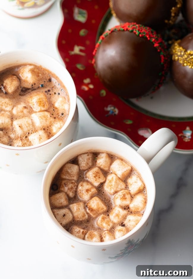 Magical Melting Cocoa 15 Two mugs of hot cocoa in Christmas mugs with plate of chocolate balls on festive plate in the background.