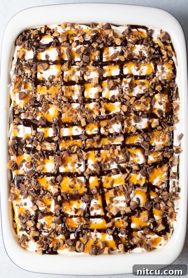 Sinfully Delicious Delight 12 Top-down view of the completed Better Than Sex Chocolate Poke Cake presented in a large white baking dish, elegantly garnished with swirls of chocolate and caramel sauce and a scattering of chopped toffee candy bars, ready to be served.