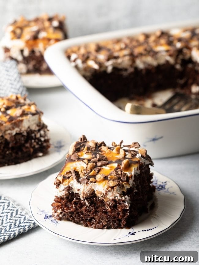 Sinfully Delicious Delight 14 A slice of Better Than Sex chocolate poke cake, generously topped with whipped cream and caramel sauce, is beautifully presented on a white and blue plate, with the full baking dish and a spatula blurred in the background, creating an enticing scene.