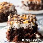 Sinfully Delicious Delight 15 Close-up view of a chocolate poke cake with whipped topping, caramel and chocolate sauce, and chopped Heath bars