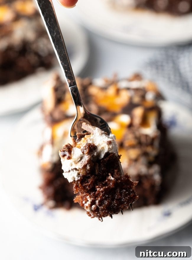 Sinfully Delicious Delight 4 A fork lifts a generous bite of chocolate cake, showcasing the distinct layers of cake, rich caramel, fluffy whipped topping, and crunchy toffee candy bar pieces, promising a delightful texture and flavor combination.