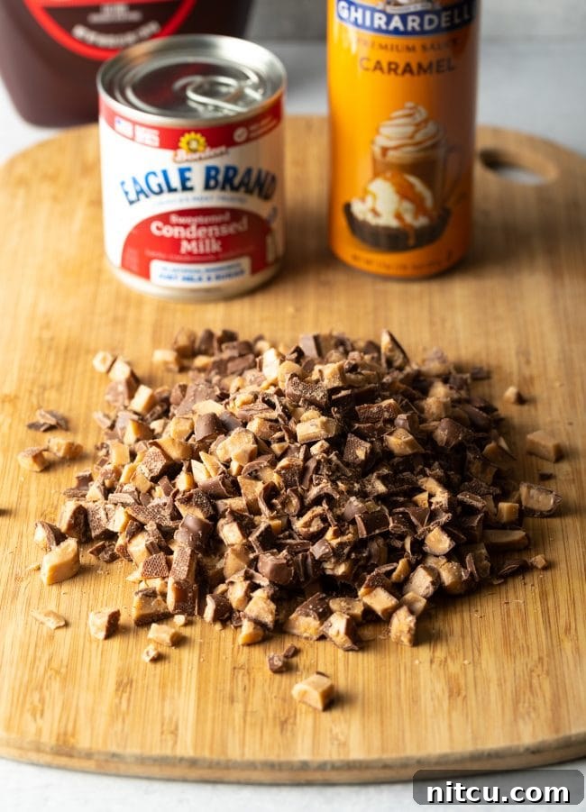 Sinfully Delicious Delight 5 A wooden cutting board holds a pile of freshly chopped toffee bars. In the soft-focus background, a can of sweetened condensed milk and a bottle of caramel sauce are visible, highlighting the key ingredients for the cake's decadent topping and soak.