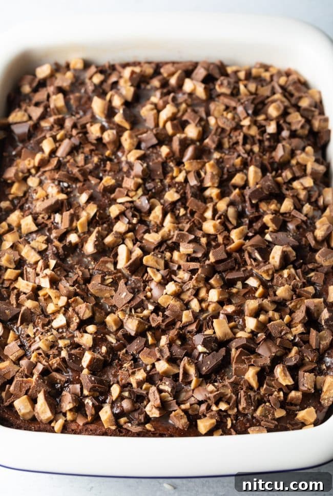Sinfully Delicious Delight 9 Top-down view of a white rectangular baking dish holding the cake, now covered with a generous layer of chopped Heath bars, signifying the next step in its preparation before chilling.