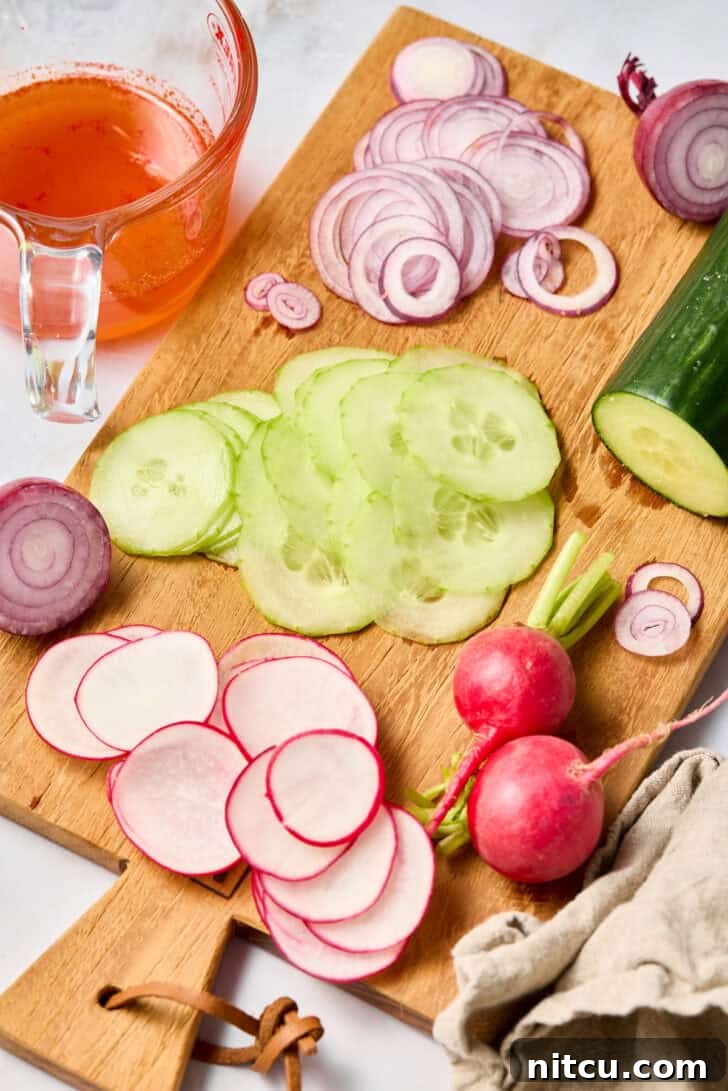 Wood cutting board with sliced cucumbers, red onions, and radishes.