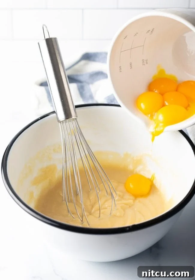 Featherlight Japanese Sponge Cake 5 adding eggs to a batter in a bowl with metal whisk
