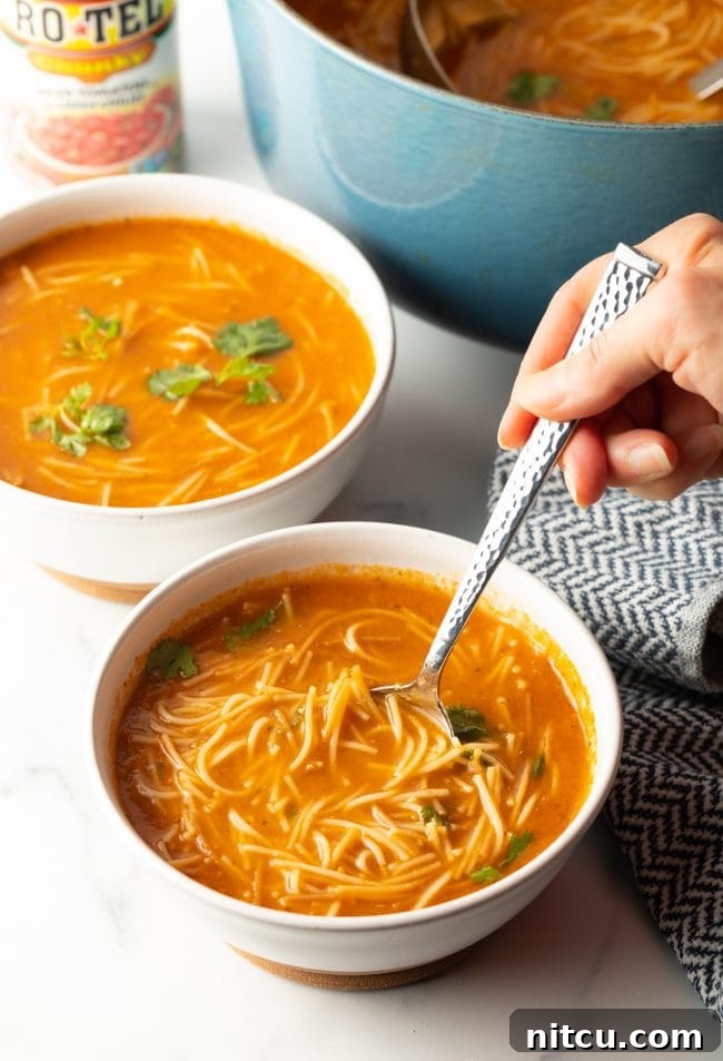Mexican Fideo Noodle Bowl 12 two bowls of sopa de fideo with a pot of soup in the background, foreground shows a hand holding a spoon scooping a bite of soup