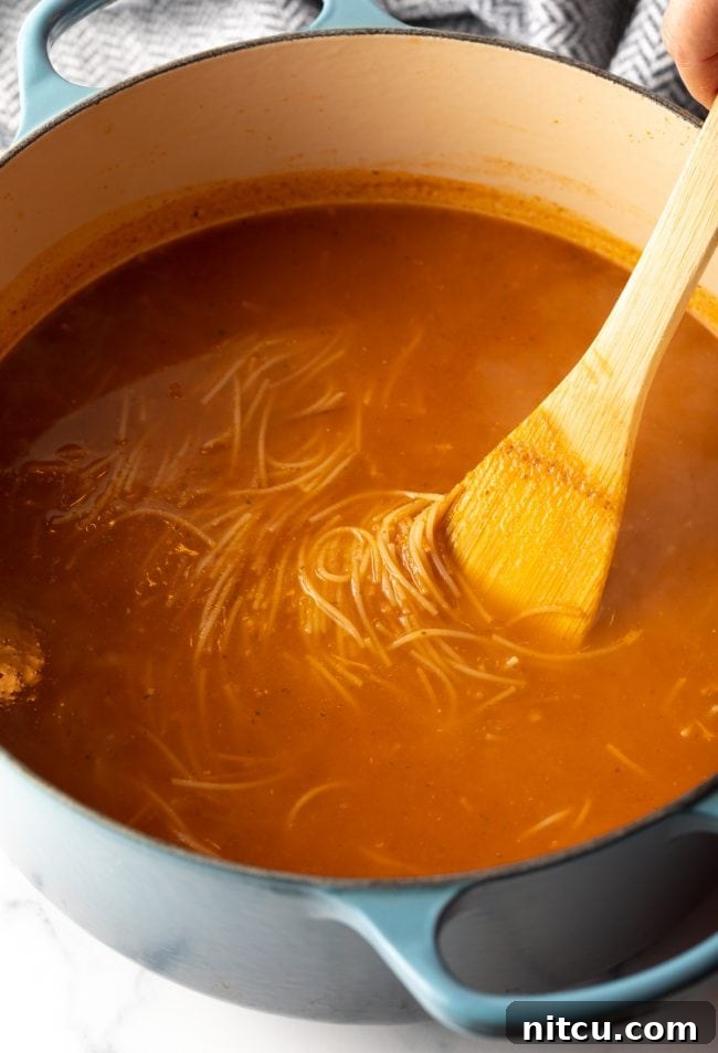 Mexican Fideo Noodle Bowl 10 wooden spoon stirring Mexican tomato soup with noodles in a large pot, illustrating the cooking process