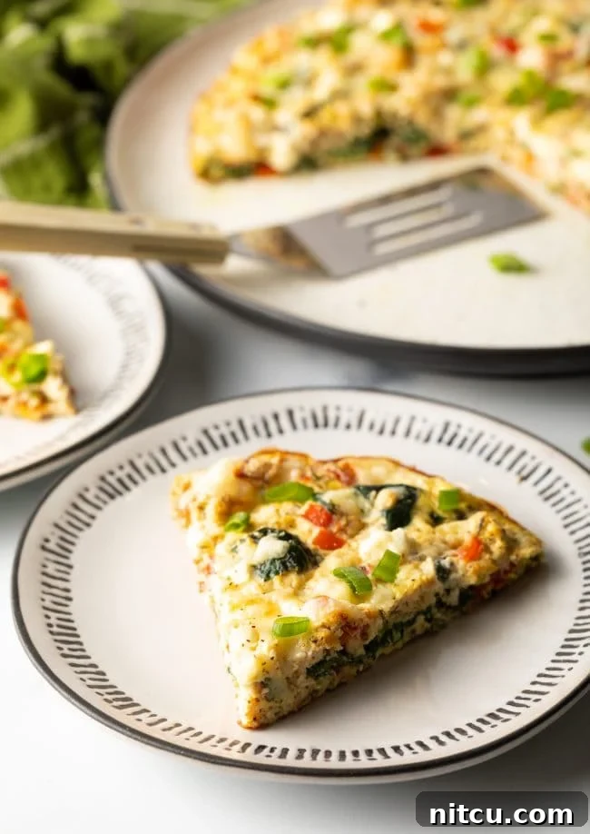 Slice of a fluffy egg white frittata with spinach and peppers on a white plate, with the full baked dish in the background