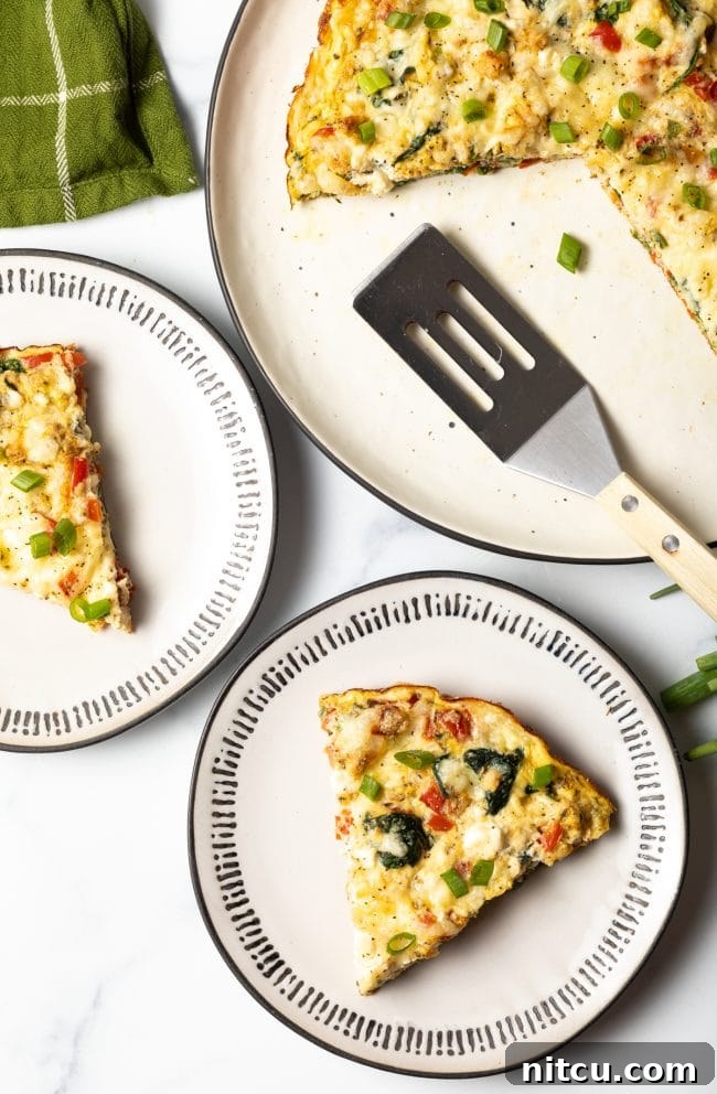 Top-down view of two plates with spinach and pepper frittata slices, with the full baked dish and a spatula in the background