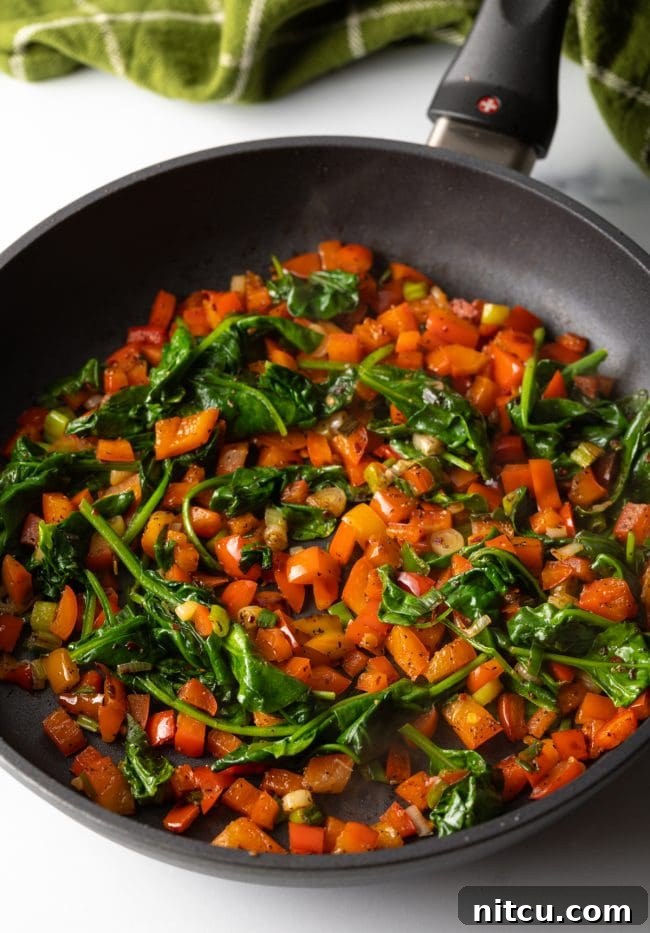 Cast iron skillet with chopped red peppers and wilted spinach being sautéed