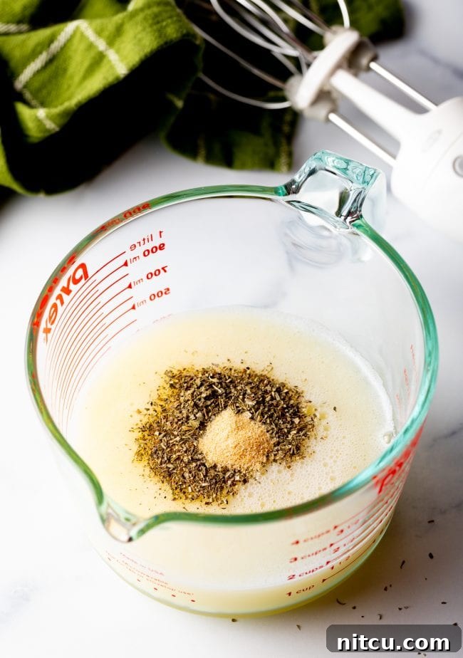 Frothy egg whites in a measuring glass with Italian seasoning and garlic powder