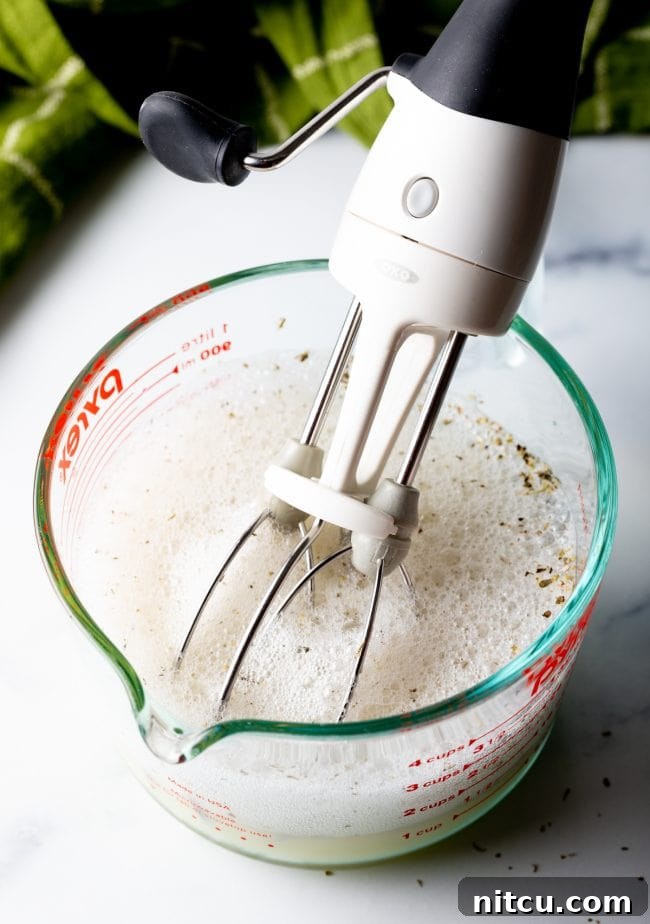 Using a hand mixer to beat egg whites and seasonings in a measuring glass until frothy