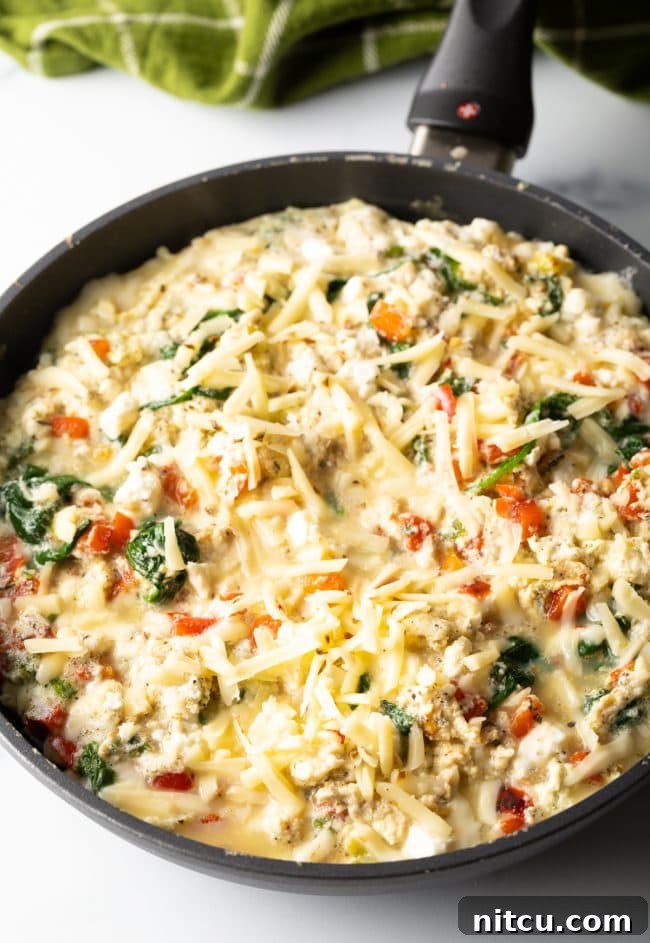 Unbaked frittata in a cast iron skillet with feta and pepper jack cheese sprinkled on top