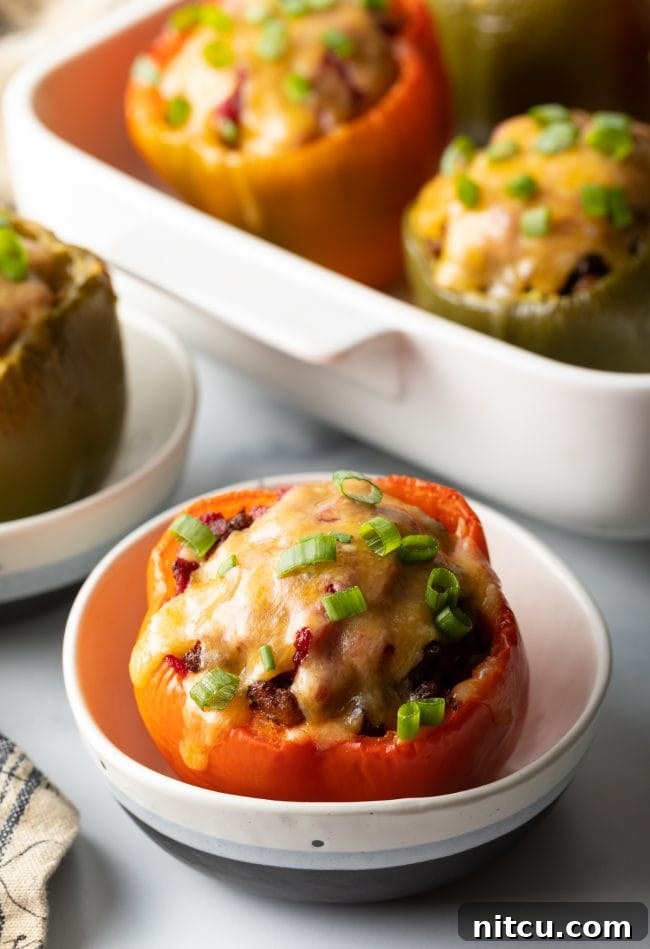 Savory No Rice Keto Beef Stuffed Peppers 2 Red bell pepper stuffed with ground beef, topped with melted cheese and chopped scallions, set in a white bowl.