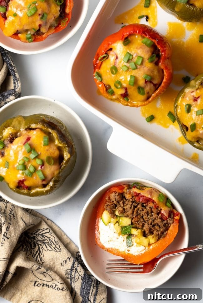Savory No Rice Keto Beef Stuffed Peppers 12 Top view keto stuffed peppers, one cut in half to show ground beef, zucchini, and cream cheese, set in a white bowl.