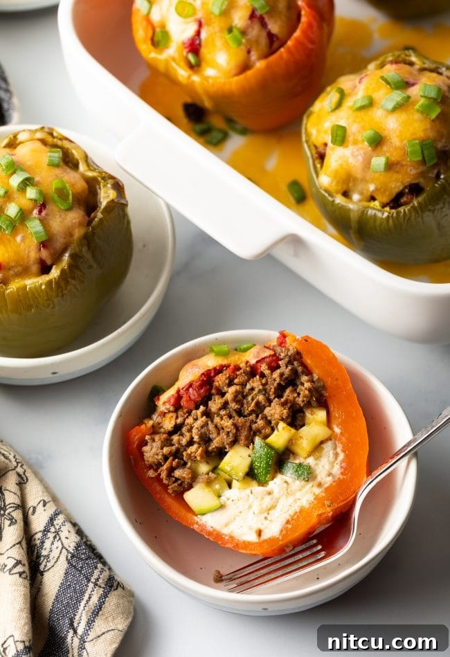 Savory No Rice Keto Beef Stuffed Peppers 3 Top view keto stuffed peppers without rice, one cut in half to show ground beef, zucchini, and cream cheese, set in a white bowl.