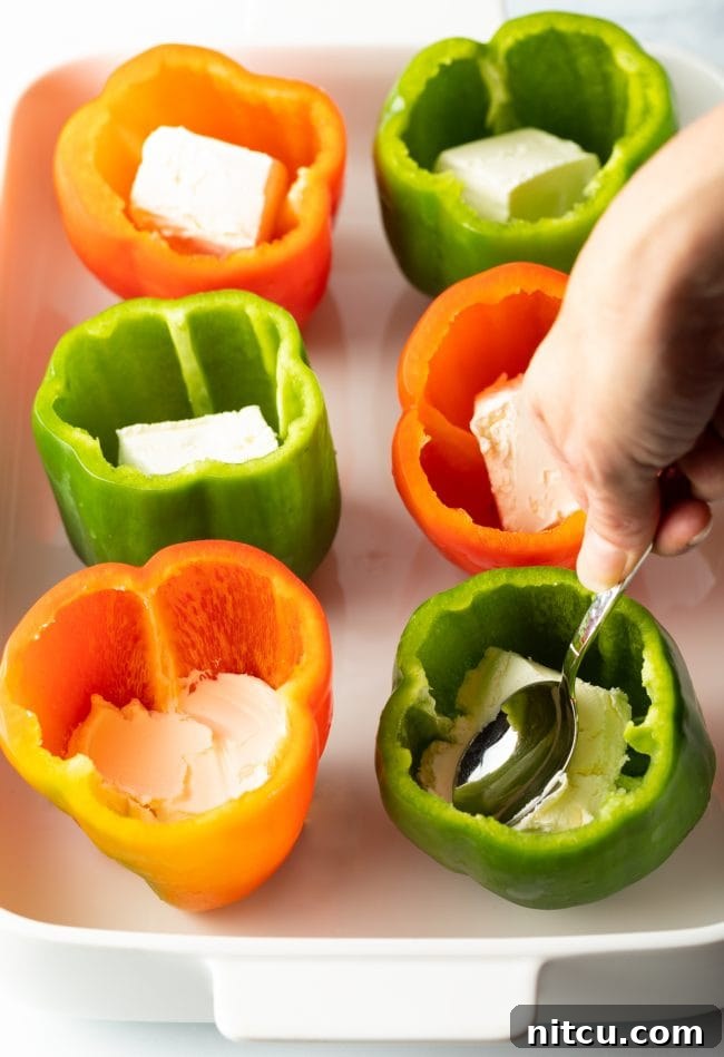 Savory No Rice Keto Beef Stuffed Peppers 6 Hand using a spoon to press cream cheese into each pepper cavity.