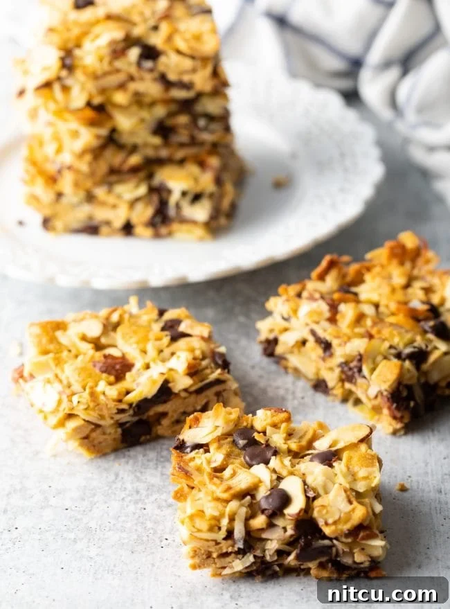 Several squares of keto cereal treats with coconut and nuts arranged on a gray background.