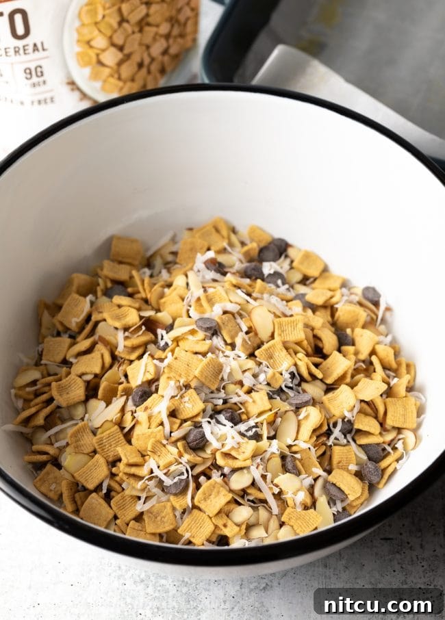 Keto cereal, chocolate chips, shredded coconut, and sliced almonds mixed in a large white mixing bowl.