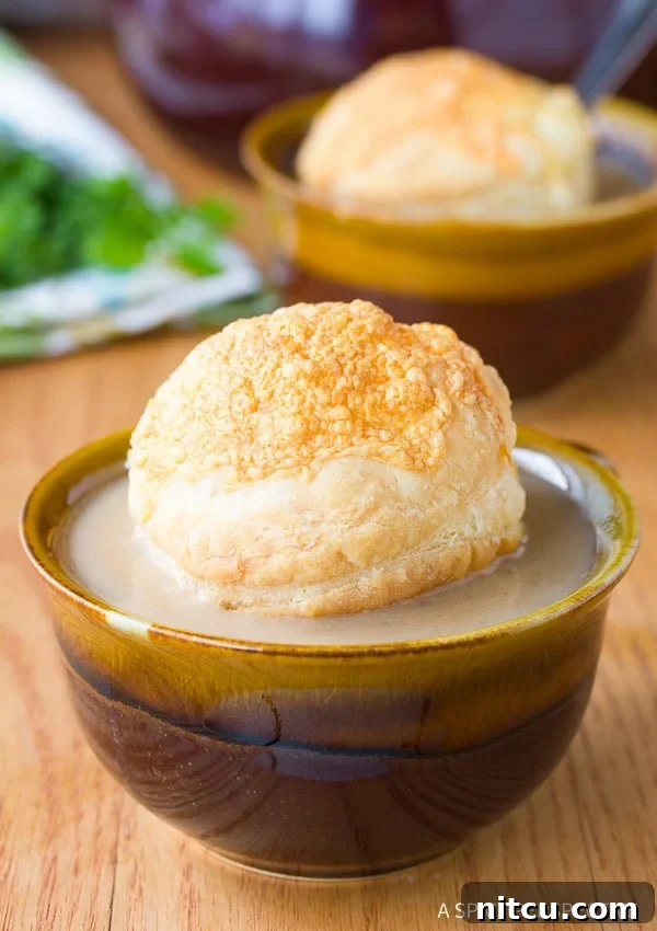 A steaming bowl of creamy French onion soup, topped with a golden, flaky cheese pillow.