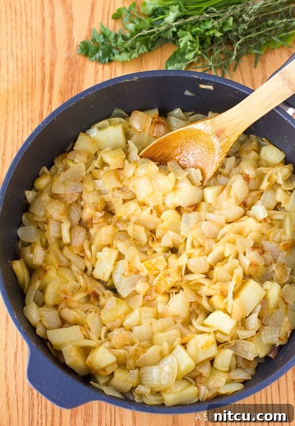 Close-up of onions slowly caramelizing in a sauté pan, turning golden brown.