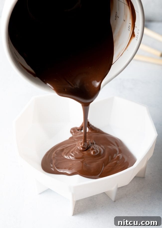 Crackable Chocolate Treasure 7 Melted chocolate is expertly poured from a white measuring cup into a flexible white silicone heart shell mold, ensuring a perfect coating.