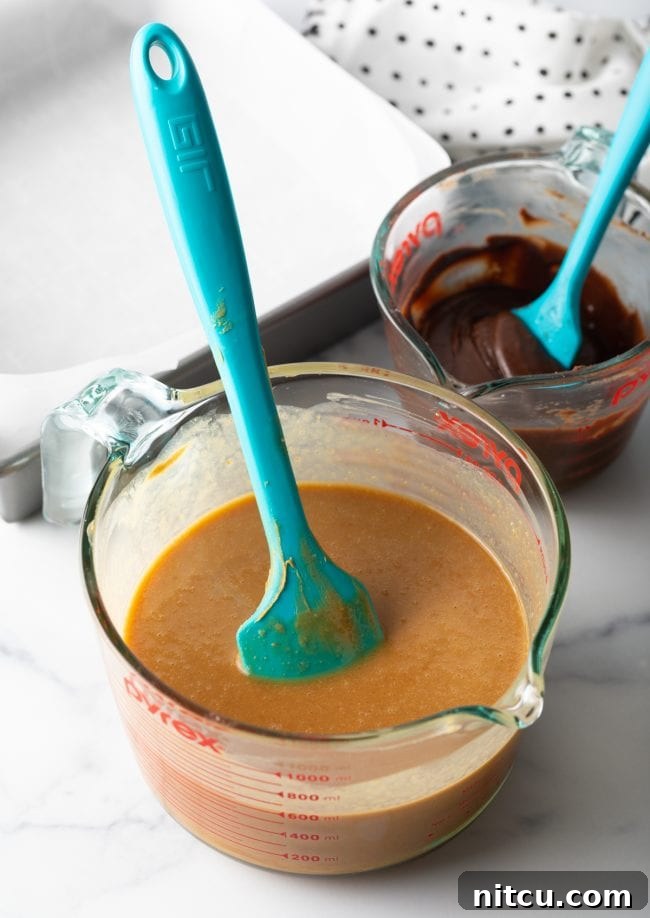 Peanut Butter Delights 7 Melted peanut butter mixture in a clear glass mixing cup, ready for the next step, with a blue spatula.