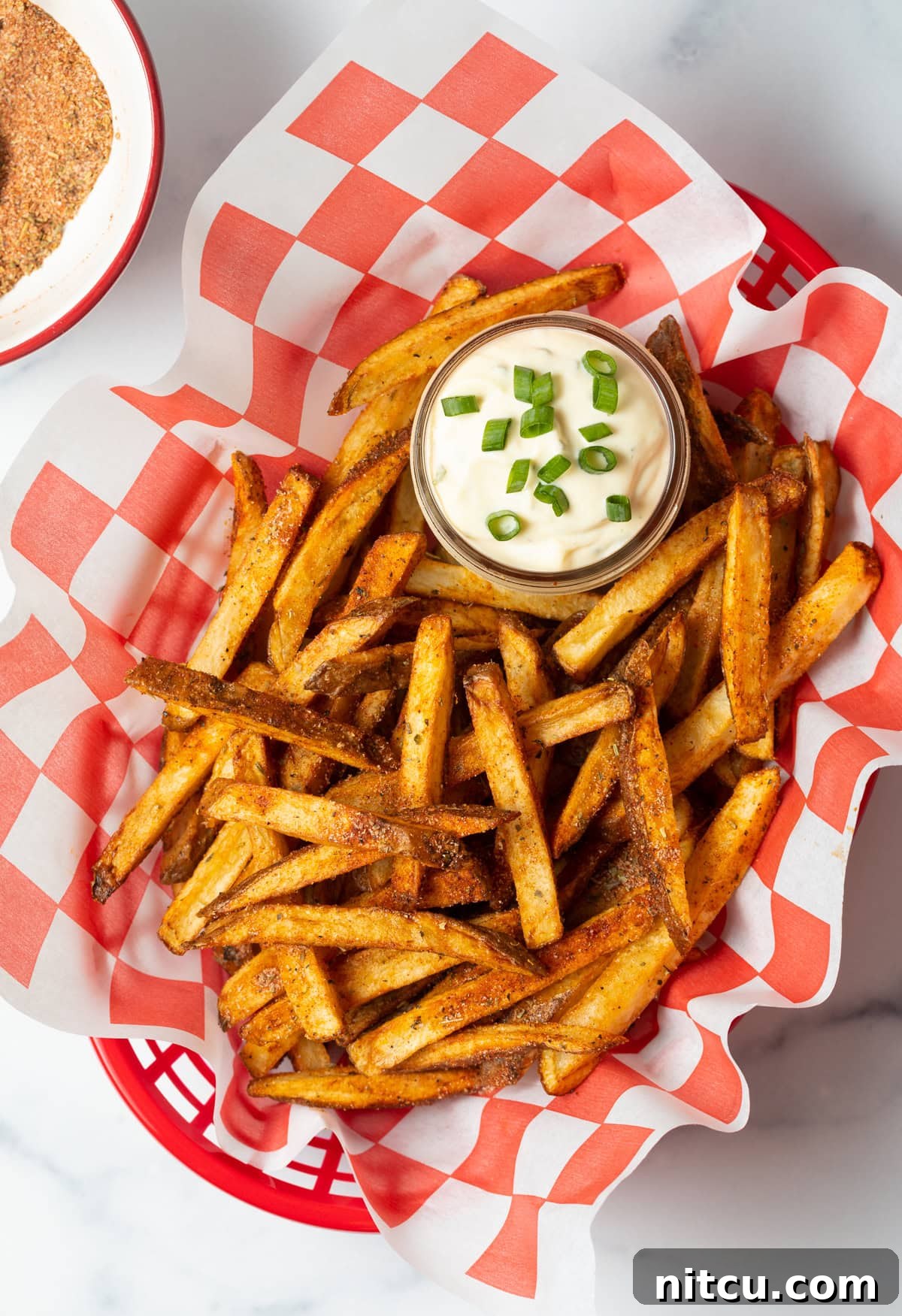 Cajun Fries: Homemade Seasoning Blend Recipe 4 Top view spicy Cajun fries in a basket with sauce in a small cup of sauce.