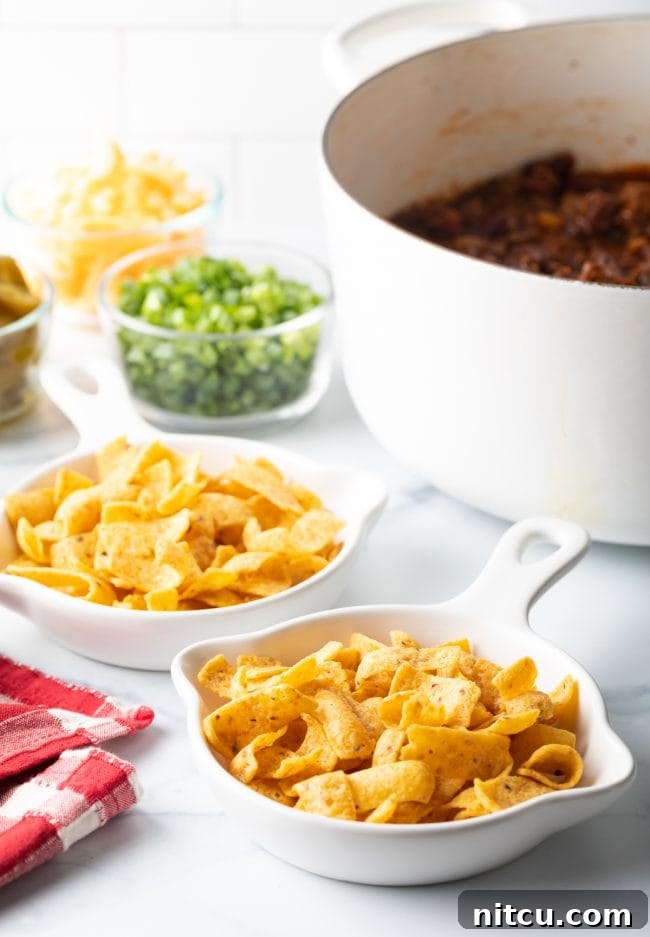 Ultimate Frito Chili Pie 4 A vibrant spread of Fritos corn chips in shallow dishes, with a variety of fresh toppings arranged neatly in the background.