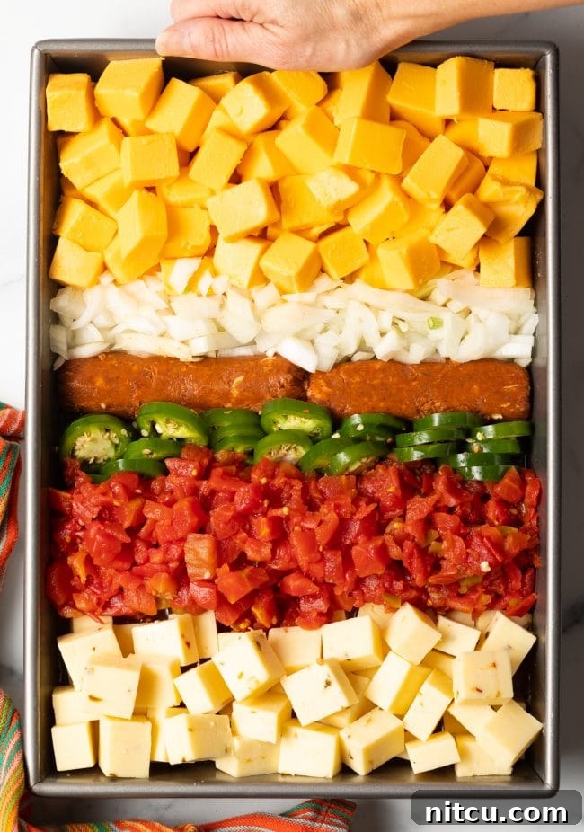 Pitmaster's Smoked Queso 5 Top view of a metal pan filled with rows of pepper jack cheese, Rotel, sliced jalapeños, Mexican chorizo, diced onions, and Velveeta cubes, ready for smoking.