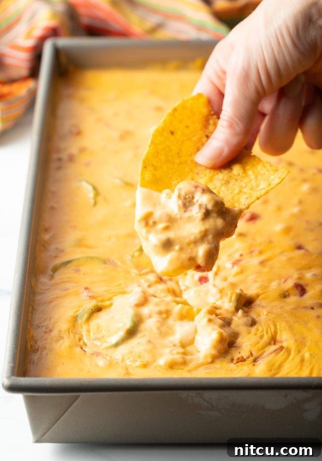 Pitmaster's Smoked Queso 8 A hand with a tortilla chip scoops rich Mexican chorizo smoked queso cheese dip from a metal pan, highlighting its creamy texture.