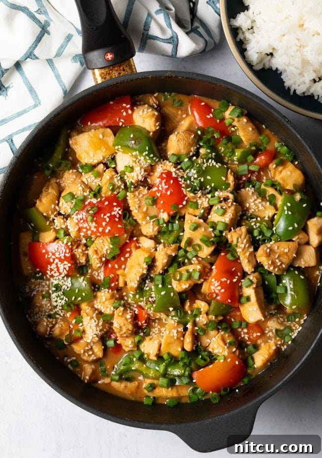 Top view finished skillet of cooked chicken and peppers, topped with sliced scallions and sesame seeds.