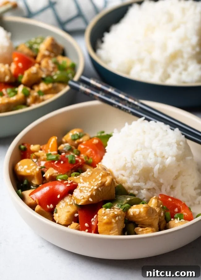 Bowl of Chinese garlic chicken with peppers and a scoop of white rice.
