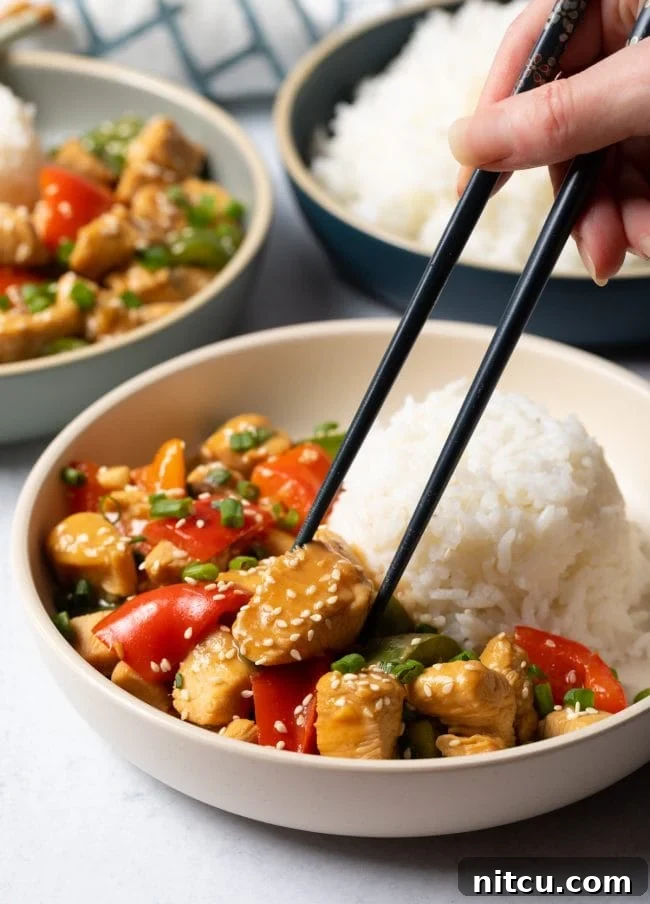 Hand with chopsticks grabbing piece of chicken from the bowl.