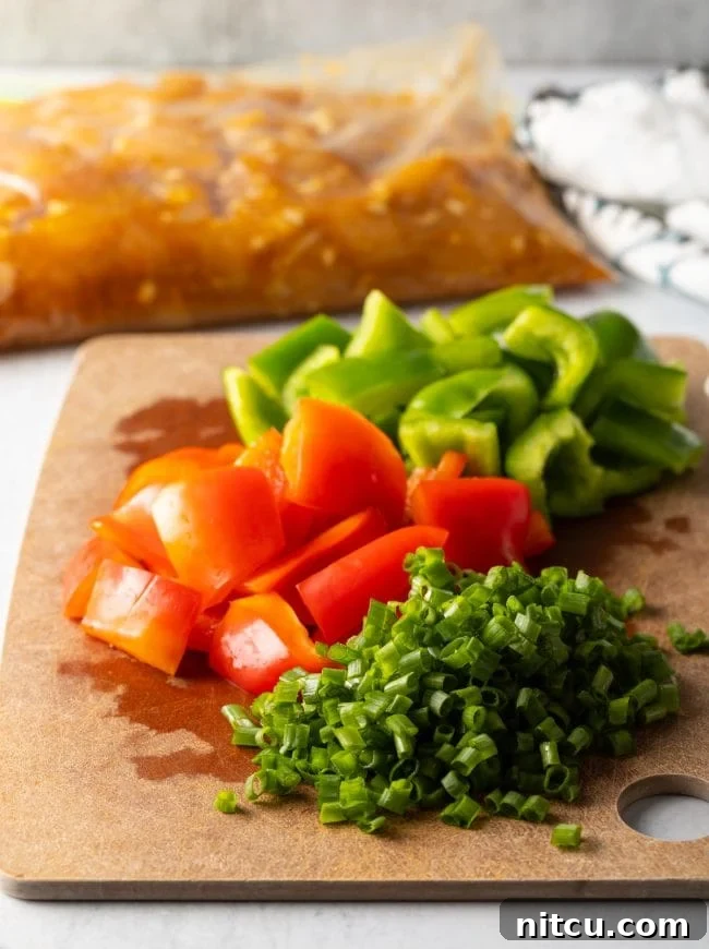 Cutting board with chopped red and green bell peppers, plus sliced scallions.